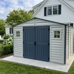 Duramax RidgeLine 10.5 x 10.5 vinyl storage shed installed beside a home in a landscaped backyard